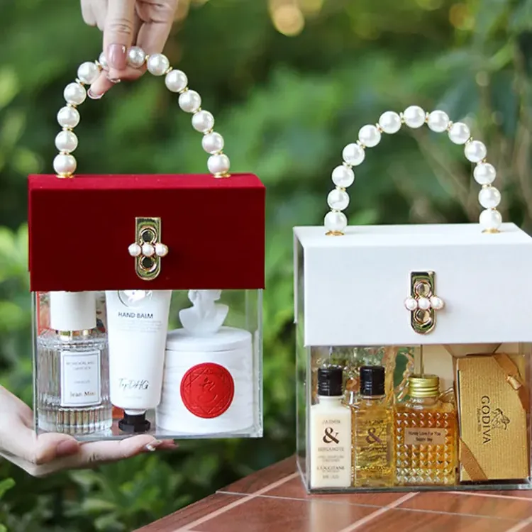 Two clear acrylic handbag-style boxes with hinged lids and pearl handles, holding gift bottles