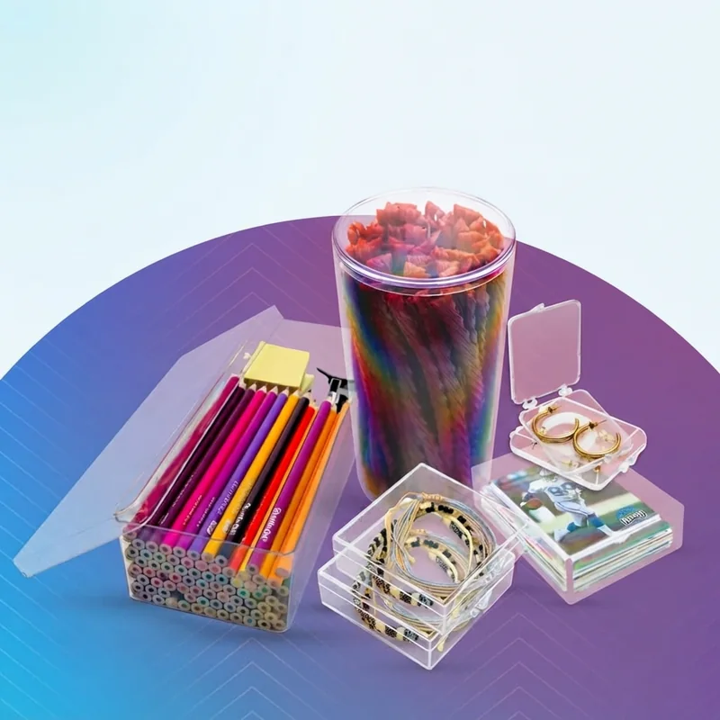 A set of clear acrylic lidded trays holding colored pencils and pens, photographed on a lilac background