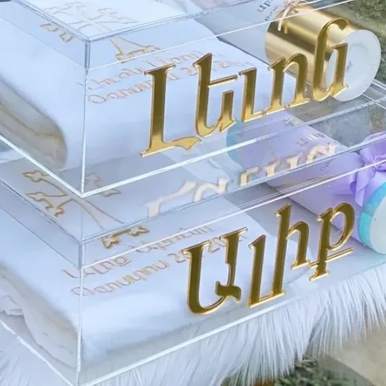 Gold metal lettering standing proud of the front face of two stacked clear acrylic boxes