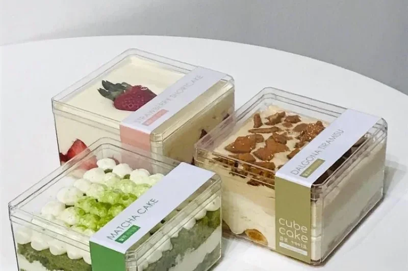 Clear acrylic boxes holding pastries and small cakes on a white table