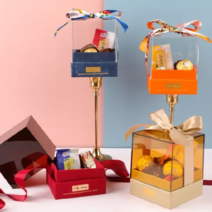 A row of clear acrylic gift boxes on colored bases, each tied with a ribbon, against a two-tone backdrop