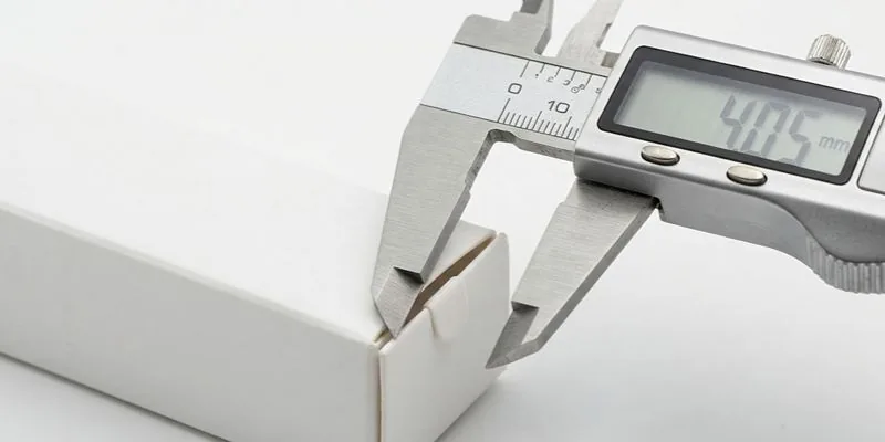 A digital caliper measuring the corner of a white box, reading 4.05 mm