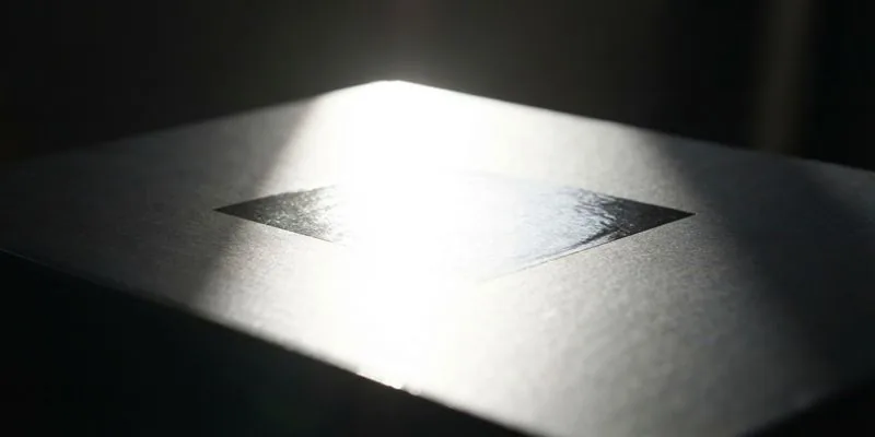 A dark close-up of a box corner under raking light showing a glossy foil panel