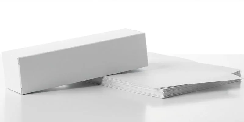 A blank white folding carton beside a stack of unprinted white label sheets