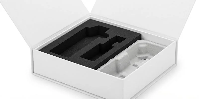 An open white box with a black foam insert beside a molded paper-pulp tray