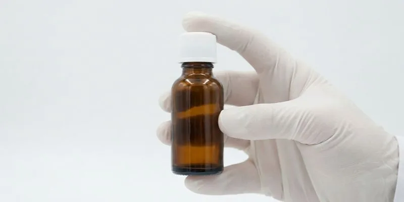 A gloved hand holding an unlabeled amber e-liquid dropper bottle