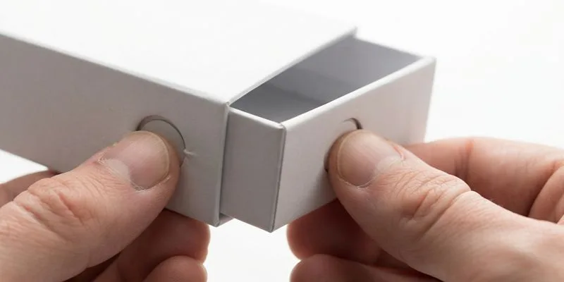 Two hands pulling a white child-resistant slide box open by its thumb notches