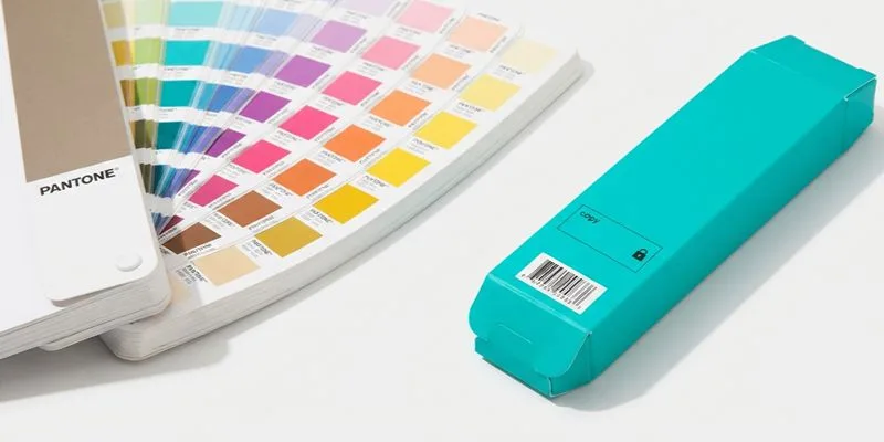 A Pantone color fan deck beside a teal vape carton with a printed barcode
