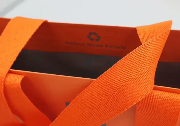 A soft woven cotton tape handle attached to a cream paper bag