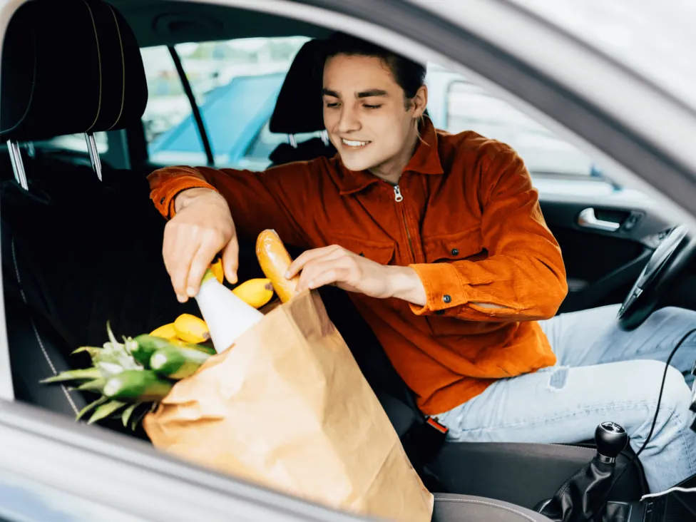 A man loading a paper grocery bag into the open boot of a car