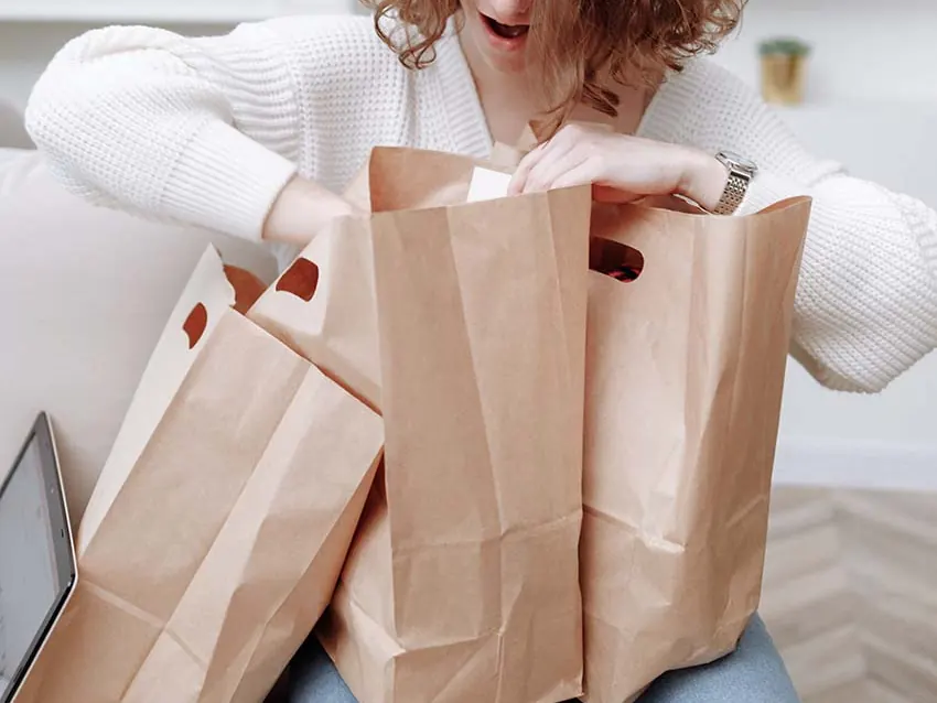 A woman sitting on a sofa with several kraft paper bags around her