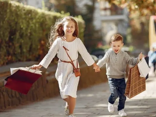 Two children walking outdoors, each carrying a paper bag