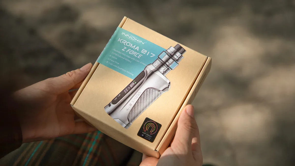 A hand holding a slim printed vape carton