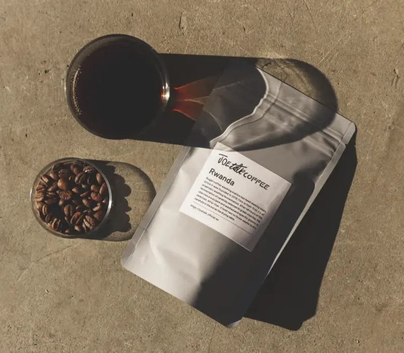 A kraft coffee pouch standing beside a scatter of roasted beans