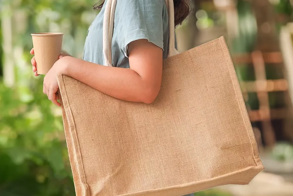 A shopper carrying a large natural jute reusable shopping bag with cotton rope handles