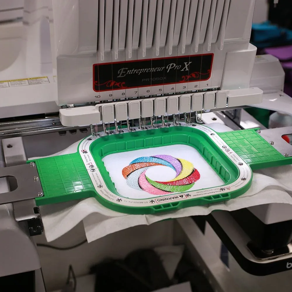 A ten-needle embroidery machine stitching a multicolor swirl onto white fabric