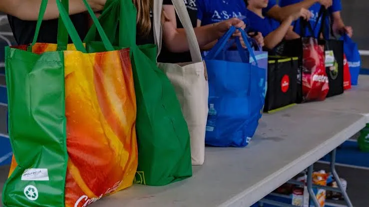 Shoppers at a collection counter holding printed reusable bags in green, orange and blue