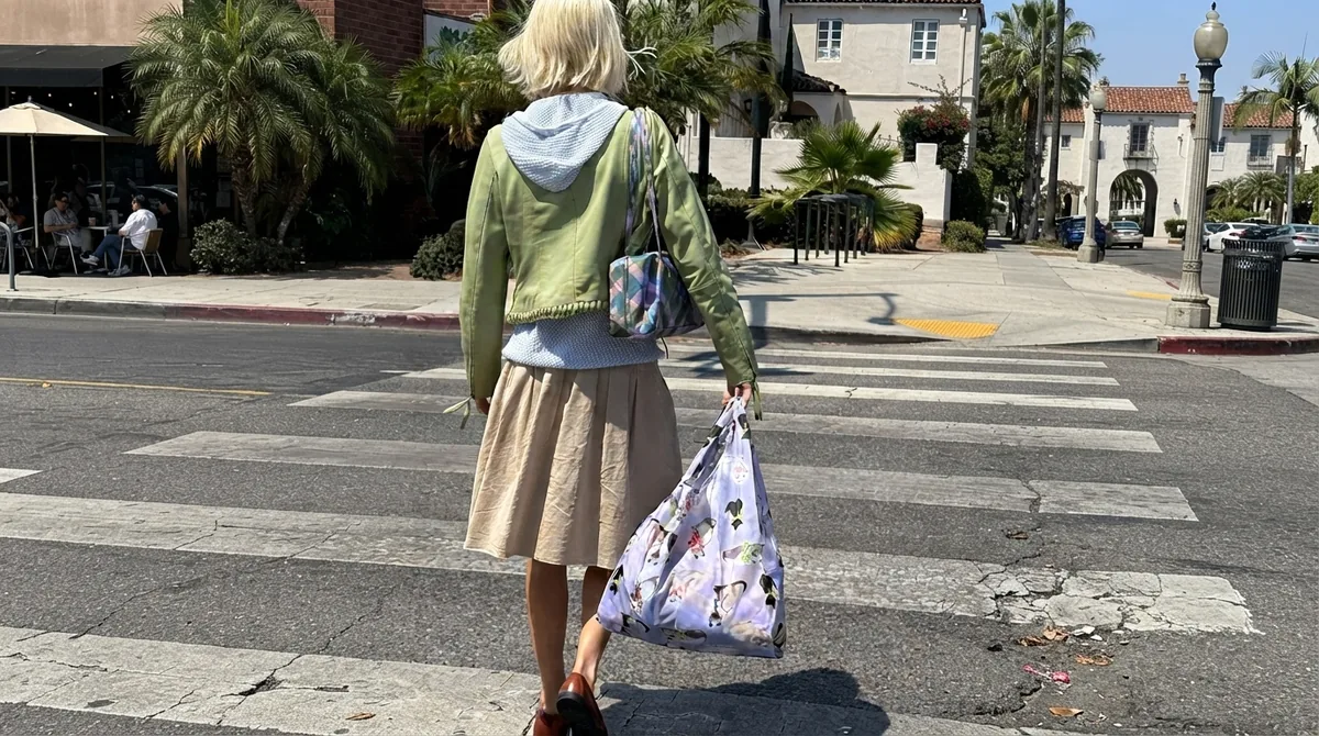 A shopper crossing a sunlit street carrying a printed boutique shopping bag