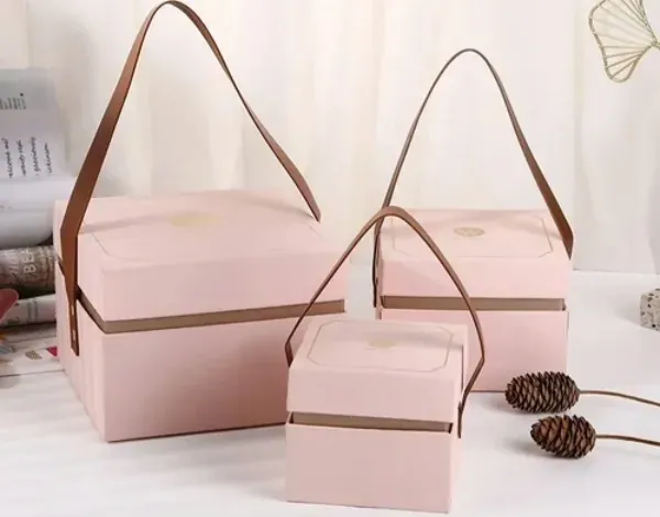 Two pink rigid boxes with tan leather handles and printed lids